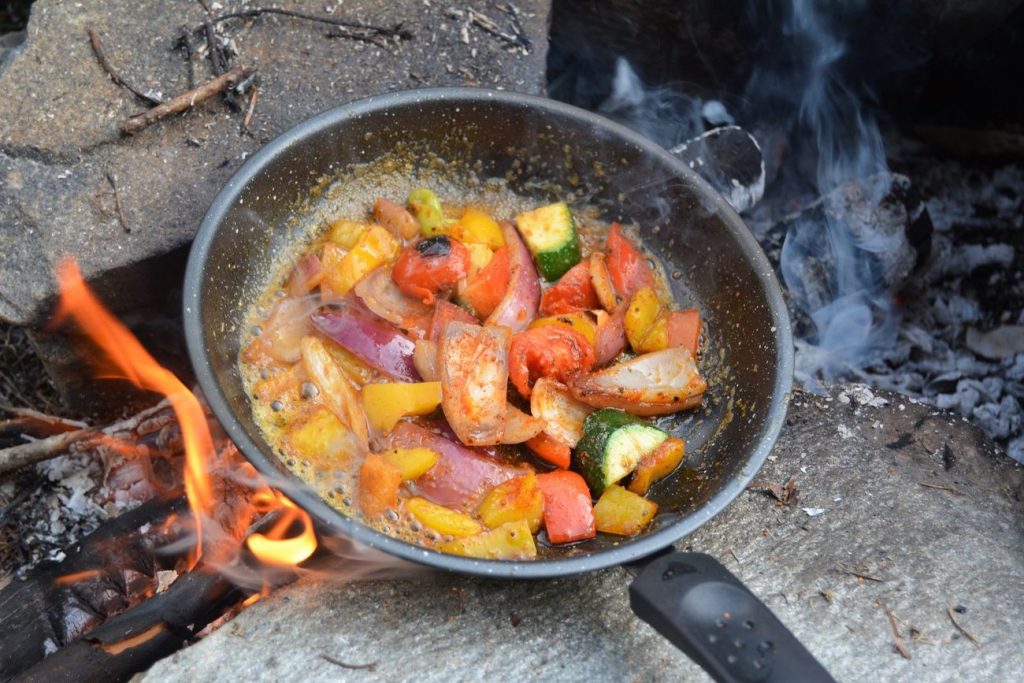 Vegetables cooking in a skillet over a campfire