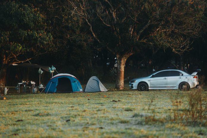 Two tents and a car parked under trees at a campground